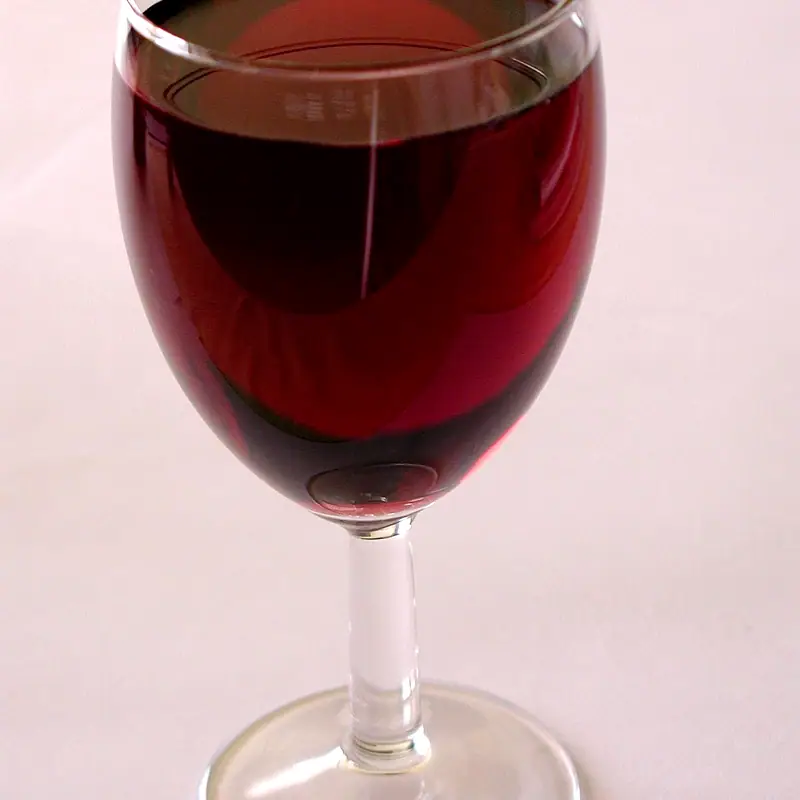 A stemmed glass filled with deep red wine, against a plain pale background