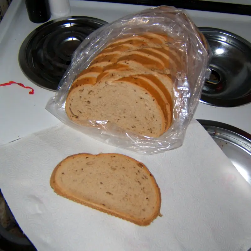 A sliced loaf of rye bread in an unbranded plastic bag, with a slice cut in front