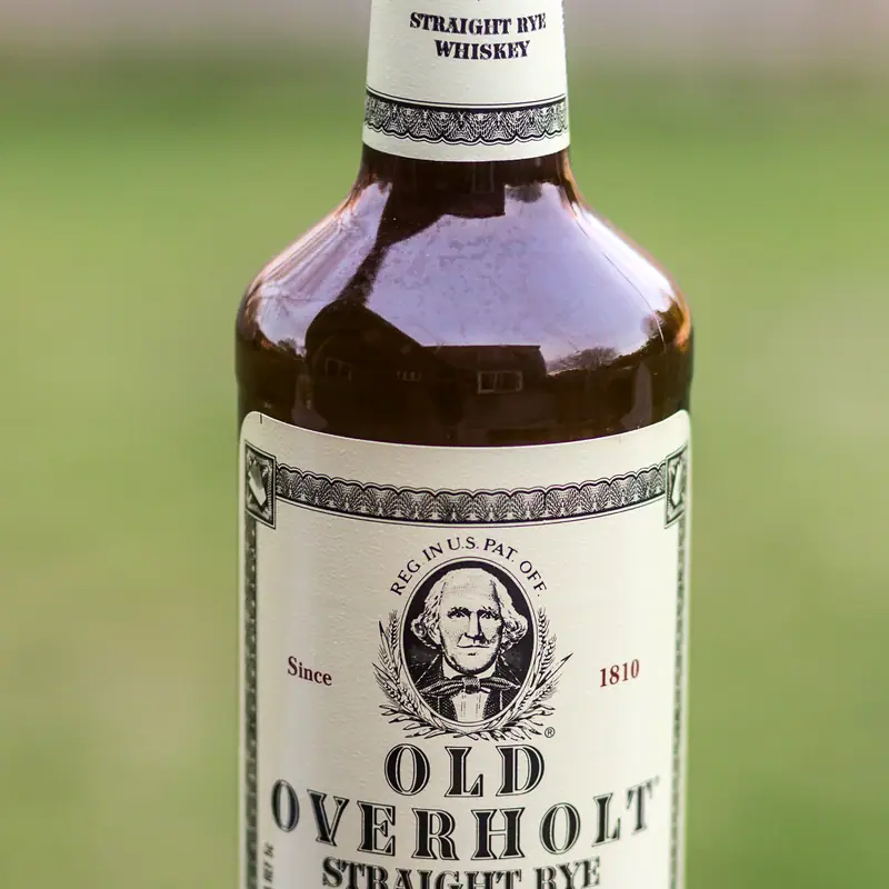 A bottle of Old Overholt Straight Rye Whiskey, showing its cream label with the founder's portrait