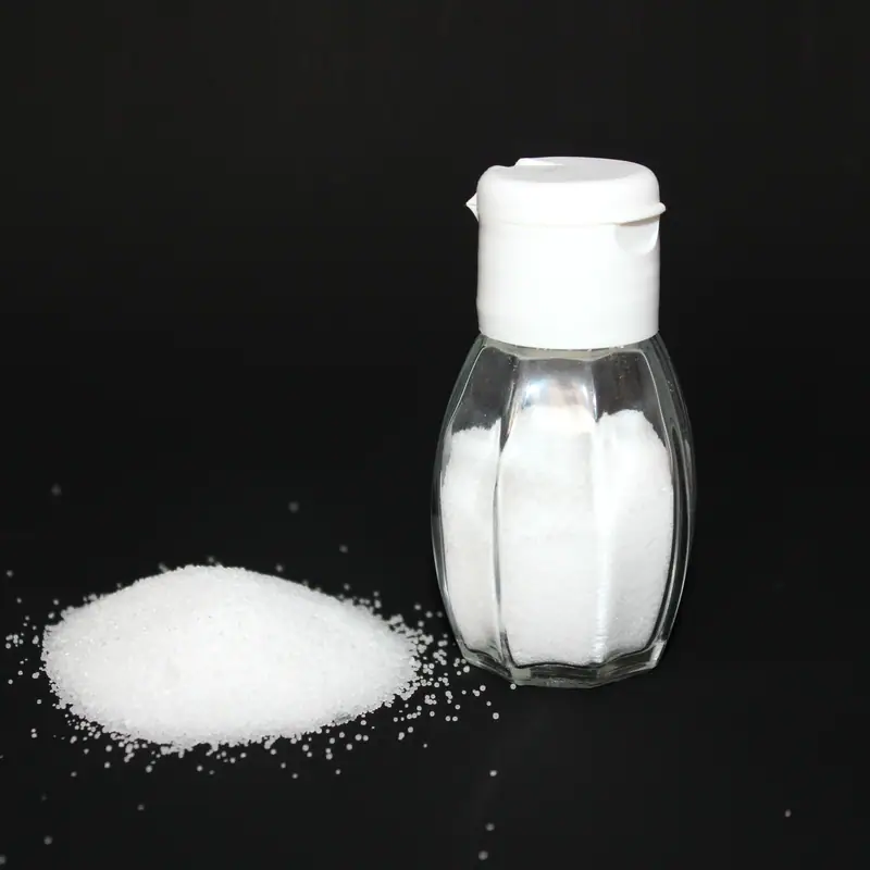 A glass salt shaker on a black ground with a small heap of fine white salt spilled beside it
