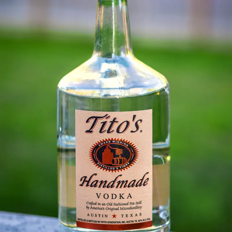A large bottle of Tito's Handmade Vodka against a blurred outdoor background
