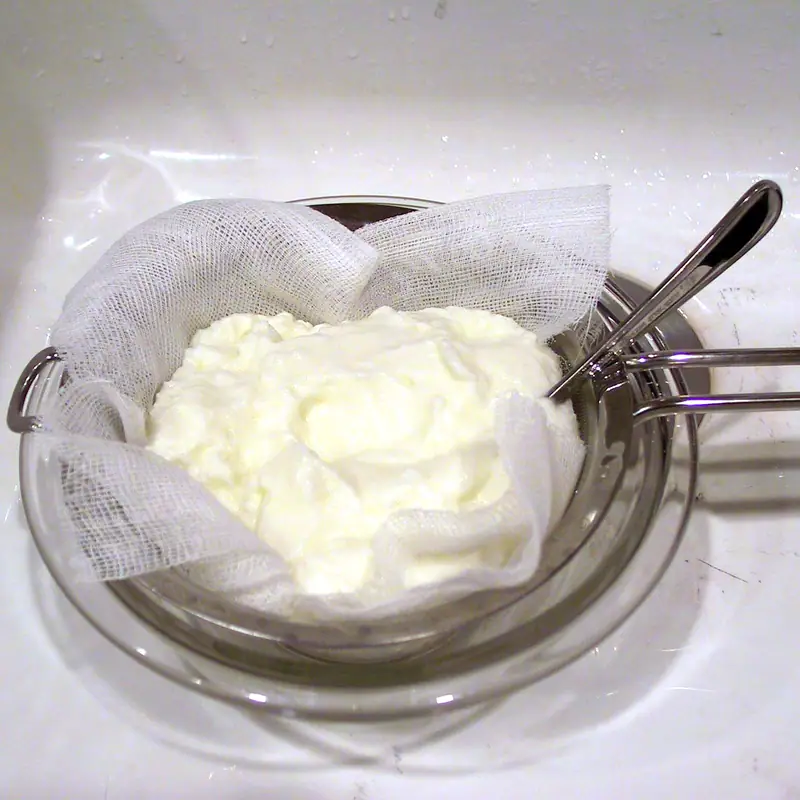 Thick white yoghurt straining through cheesecloth into a glass bowl