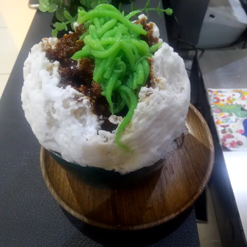 Curly green cendol jelly strands piled on shaved ice in a bowl