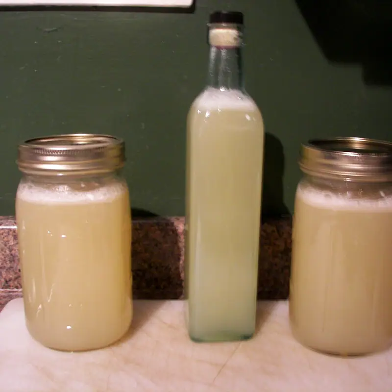 Jars and a bottle of cloudy pale orgeat standing on a kitchen counter