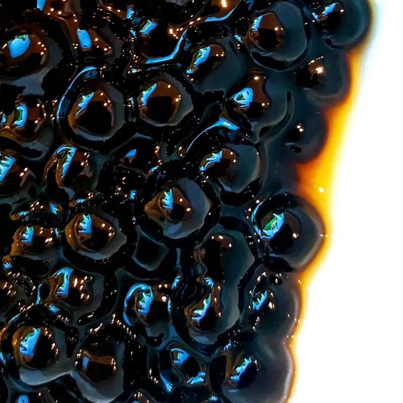 A tight close-up of glossy, dark brown cooked tapioca pearls